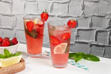 Refreshing drink with strawberries, mint, lemon and ice on white table against grey textured...
