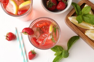 Refreshing drink with strawberries, mint, lemon and ice on white table, flat lay