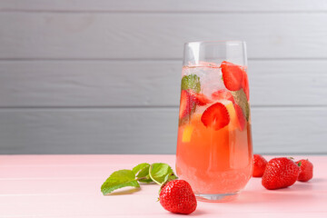 Refreshing drink with strawberries, mint and ice on pink wooden table against grey background,...