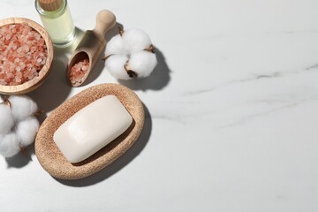 Soap bar, cosmetic products and cotton flowers on white marble table, flat lay. Space for text
