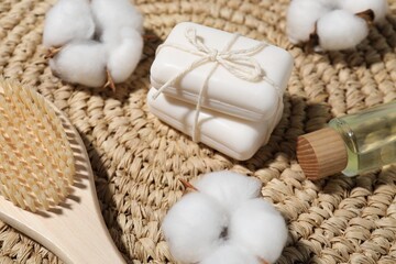 Soap bars, cotton flowers, cosmetic product and brush on wicker mat, closeup