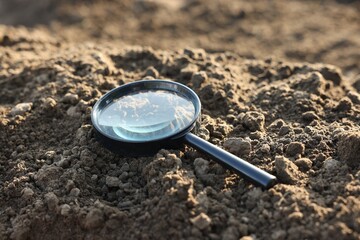 Magnifying glass on dry soil in field, closeup