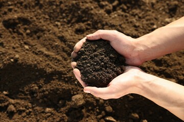 Man holding pile of soil in field, top view. Space for text
