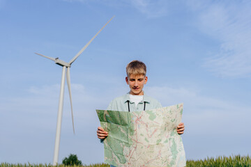 Teen boy reading map near wind turbine in countryside landscape