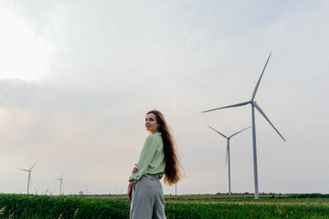 Confident woman in countryside near wind turbines, looking at camera