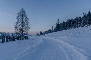 Snow-covered landscape with a winding path leading through a serene winter scene, featuring tall...