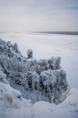 Snow-covered rocky cliffs rise above a frozen river, showcasing the stark beauty of winter...