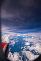 A stunning aerial view of clouds and the landscape below, captured from an airplane window. The...