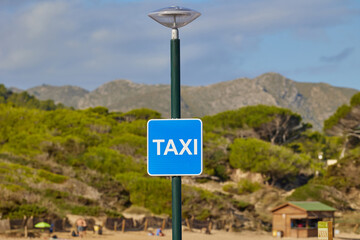 Blue taxi sign at beachside location with forest and mountains in the background on a sunny day