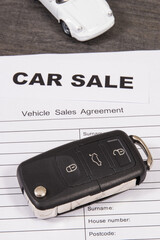 White toy car, car key and form of vehicle sales agreement. Inscription car sale. Sales or purchases new or used vehicle