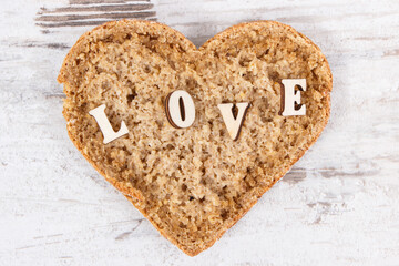 Wholegrain bread in shape of heart for breakfast and inscription love. Old rustic background