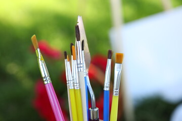 A colorful collection of paint brushes stands in a holder, surrounded by vibrant flowers and...