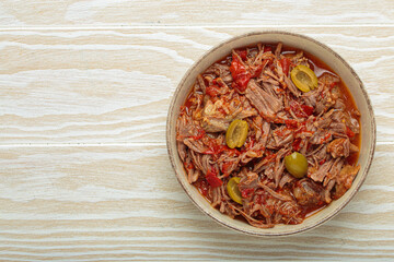 Ropa vieja, a traditional Cuban dish, is served with white rice, tomato sauce, and green olives on a plate from above on white wooden background