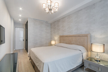 This inviting bedroom features a plush bed with soft linens, an elegant chandelier, and tasteful decor that creates a relaxing ambiance for restful nights.