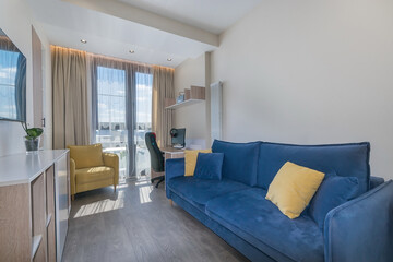 This space features a blue sofa with yellow cushions, a yellow armchair, and a desk area. Abundant...