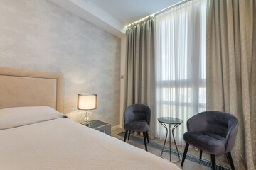 Stylish bedroom features a cozy bed with soft linens, two plush chairs, and ample natural light...