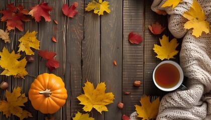 A warm and inviting arrangement features a small pumpkin, a cup of tea, and vibrant autumn leaves scattered on a rustic wooden table, creating a seasonal atmosphere.