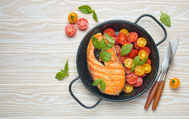 Grilled salmon steak on a black pan, accompanied by vibrant cherry tomatoes and fresh basil leaves,...