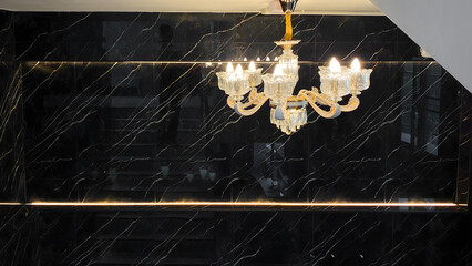Elegant Crystal Chandelier with Golden Accents Reflected on Glossy Black Marble Wall in Modern Interior Staircase