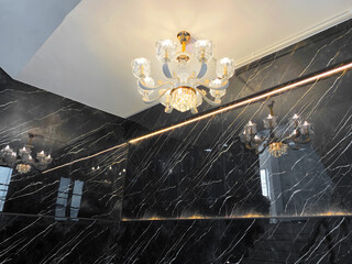 Elegant Crystal Chandelier with Golden Accents Reflected on Glossy Black Marble Wall in Modern Interior Staircase