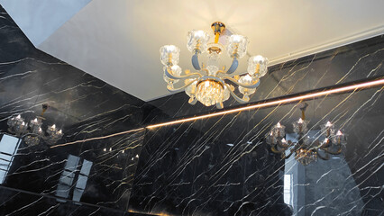 Elegant Crystal Chandelier with Golden Accents Reflected on Glossy Black Marble Wall in Modern Interior Staircase