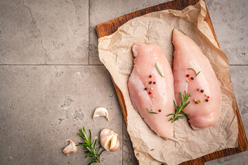 Raw chicken fillet or breasts with ingredients for cooking on a paper, gray background. Top view...