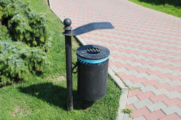 A trash can is positioned alongside a brick path in an urban setting, capturing everyday city life.