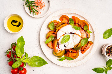 Caprese salad with burrata cheese, tomato, basil and balsamic vinegar arranged on white plate, on...