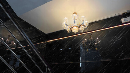 Elegant Crystal Chandelier Illuminating a Modern Luxury Staircase with Black Marble Wall and Stainless Steel Railing