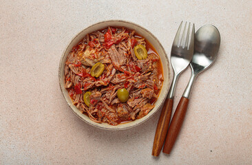 Ropa vieja, a traditional Cuban dish, is served with white rice, tomato sauce, and green olives on...