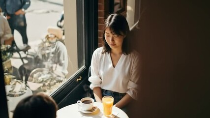 The top video of an unrecognizable woman sitting in the cafe, having a coffee and fresh orange juice on the table. - Powered by Adobe
