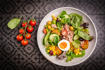 Tuna salad with tomatoes, cucumber, corn, olives , eggs and onion on black tiles background, top view. High quality photo