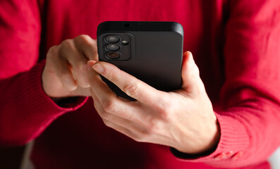 Hands of a woman holding a mobile phone in red informal clothes. Communication and social networking concept.