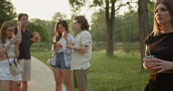 Friends enjoying a sunny day outdoors are engrossed in their smart phones, with one person feeling excluded. This illustrates the modern phenomenon of digital disconnect impacting social gatherings.