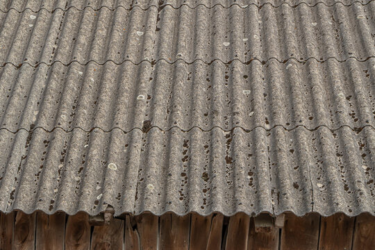 Old weathered asbestos cement roof sheets with signs of decay and aging. Hazardous building material close-up. Industrial and environmental concept