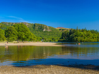People enjoy a tranquil summer afternoon on Derwentwater lakeside (Keswick, Lake District, England, United Kingdom)