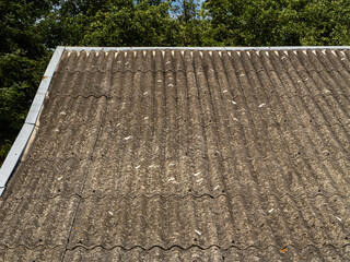 Old asbestos corrugated roof sheets on a building, showing signs of age and pollution. Toxic...