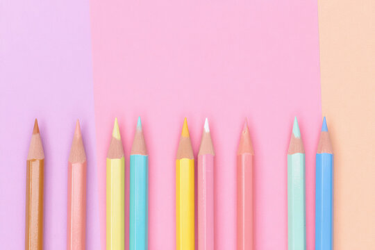 Pastel colored pencils arranged in a row on pink and peach background. Minimalist flat lay, creative art supplies, back to school, education, stationery, and design concept.

