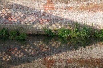 The shadow of a bridge cast upon on old brick wall, symmetrically reflected in still water on a...