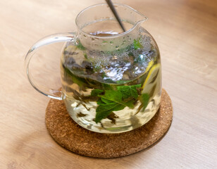 Stylish transparent tea pot with just brewed green tea leaves, mint leaves and lemon slices in it....