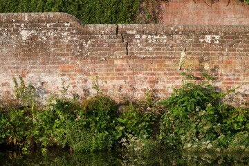 An old brick wall with structural crack. Sunny, summer afternoon beside the River Wey in Surrey,...