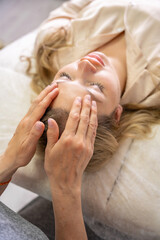 Hands of a female practitioner positioned on the face of a young woman during an Access Bars facial lifting session. Concept of energy work, healing touch and alternative face therapy