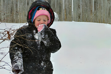 Young Girl in Winter Coat Eating Snow During a Snowfall in the Backyard

