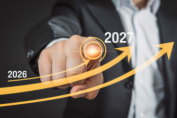 Businessman touches a futuristic interface with a glowing button, depicting growth trends with arrows from 2026 to 2027. Ideal for finance, business forecasts, and innovation concepts.