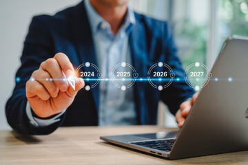 A business professional interacts with a futuristic timeline on a digital screen, highlighting the years 2024, 2025, 2026 to 2027. This symbolizes innovation and strategic planning using technology.