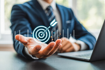 A businessman holds a glowing target icon, symbolizing precision and goal achievement. Next to him, a laptop reflects modern technology and innovation. Ideal for business success concepts.