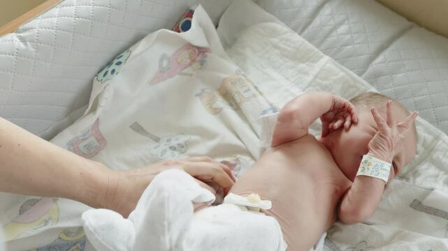 A newborn baby is being dressed with a white outfit, showcasing the delicate moment of care and the first days of life.