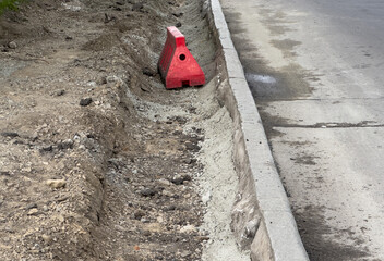 Red construction barrier rests on a dirt embankment near a freshly excavated street. Surrounding...