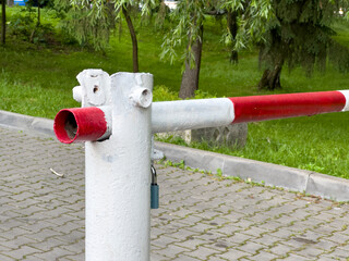 A barrier gate is positioned at the entrance of a parking area, marked with red and white stripes,...