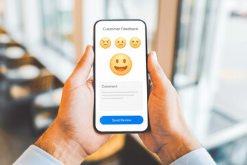 Hands holding a smartphone display a customer feedback form with happy, neutral, and angry emoticons. The comment section invites opinions, emphasizing user interaction and digital engagement.